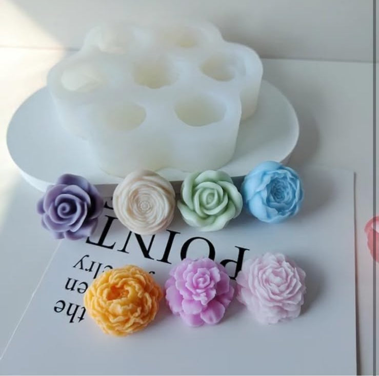 A product photo showing a white silicone mold with six cup-like cavities, alongside six small fabric or faux-fur flower shapes in assorted pastel and bright colors arranged on a white surface.