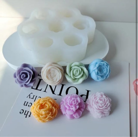 A product photo showing a white silicone mold with six cup-like cavities, alongside six small fabric or faux-fur flower shapes in assorted pastel and bright colors arranged on a white surface.
