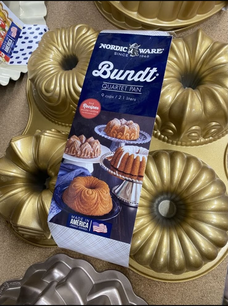 Nordic Ware Bundt pan set with a blue package in the center and several gold-colored fluted bundt pans arranged around it on a countertop.