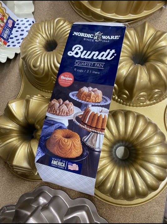 Nordic Ware Bundt pan set with a blue package in the center and several gold-colored fluted bundt pans arranged around it on a countertop.